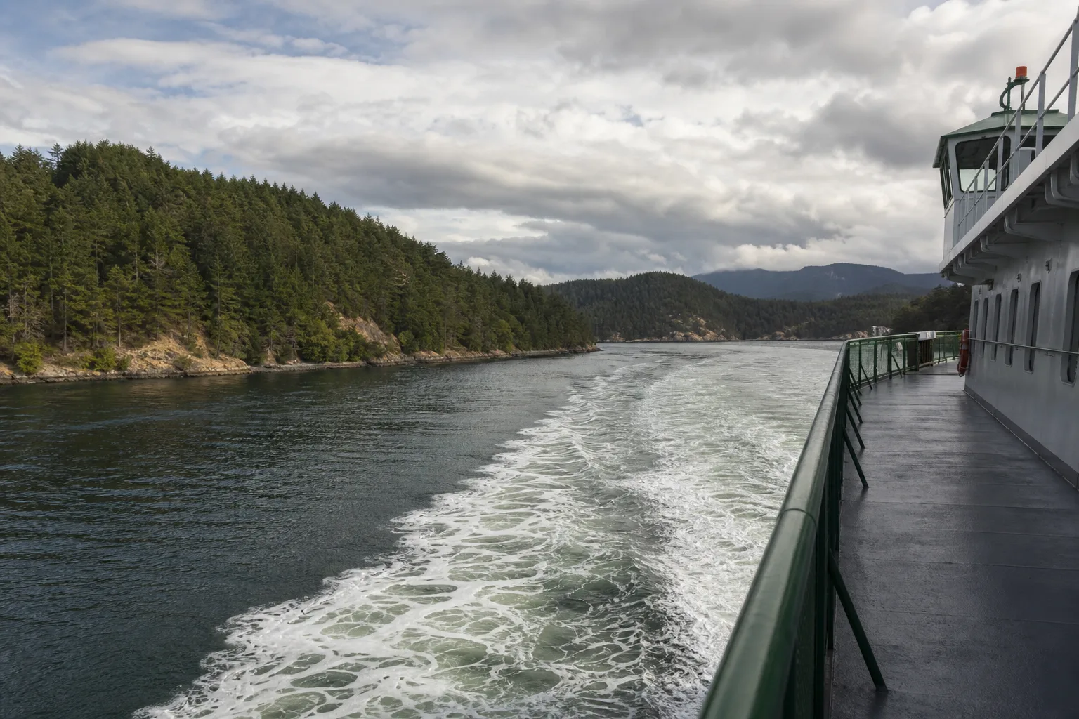 Ferry wake toward forested San Juan Islands shoreline